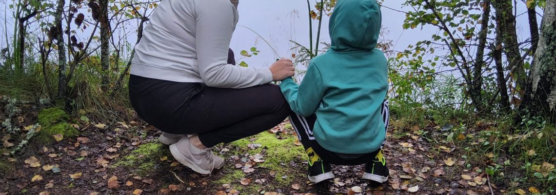 Nainen ja lapsi kyykyssä järven rannalla katselemassa järven maisemaa